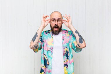 Kel adam şaşkın, şaşırmış ve şaşırmış hissediyor. Elinde şaşkın, inançsız bir bakışla gözlük tutuyor.