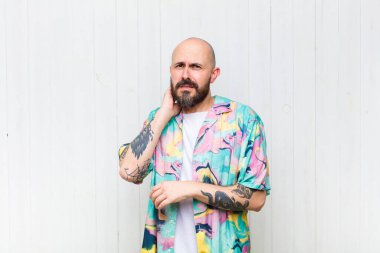 Kel bir adam stresli, hayal kırıklığına uğramış ve yorgun, endişeli ve sorunlu bir bakışla boynunu ovalıyor.