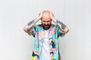 Kel adam stresli ve hayal kırıklığına uğramış hissediyor, ellerinizi havaya kaldırıyor, yorgun, mutsuz ve migren ağrısı çekiyor.