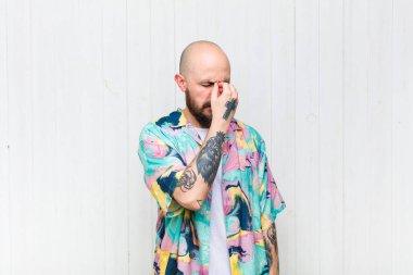 Kel bir adam stresli, mutsuz ve hayal kırıklığına uğramış, alnına dokunmuş ve şiddetli baş ağrısı çeken.