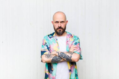 Kel adam mutsuz ve hayal kırıklığına uğramış, ciddi görünüyor, kızgın ve kollarını kavuşturmuş.