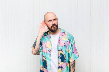 Kel adam ciddi ve meraklı görünüyor, dinliyor, gizli bir konuşma veya dedikodu duymaya çalışıyor, kulak misafiri oluyor.