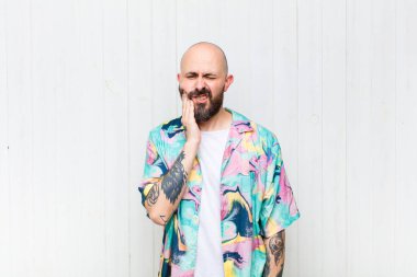 Kel adam yanağını tutuyor ve acı çeken diş ağrısı çekiyor, hasta, sefil ve mutsuz hissediyor, dişçi arıyor.