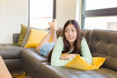 Genç Asyalı kadın kuşkulanıyor ya da düşünüyor, dudağını ısırıyor ve kendini güvensiz ve gergin hissediyor, kenarda boşluğu kopyalamak istiyor.