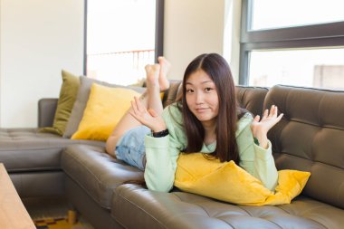 Genç Asyalı kadın şaşkın ve kafası karışık, şüpheci, farklı seçenekleri tartıyor ya da komik bir ifadeyle seçiyor.