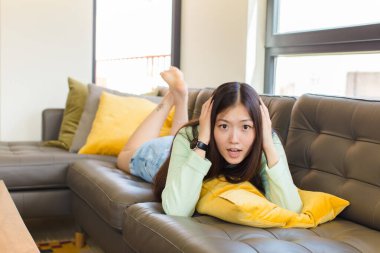 Asyalı genç bir kadın kendini stresli, endişeli, endişeli ya da korkmuş hissediyor. Elleri başının üstünde, hatayla panikliyor.