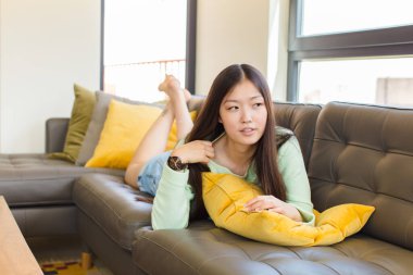 Asyalı genç bir kadın stresli, endişeli, yorgun ve hayal kırıklığına uğramış, gömleğini çekmiş, sorunlu görünüyor.