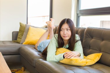 Asyalı genç bir kadın üzgün, üzgün ya da kızgın. Olumsuz bir tavır sergiliyor, anlaşmazlık içinde kaşlarını çatıyor.