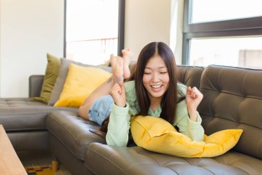 Genç Asyalı kadın son derece mutlu ve şaşırmış görünüyor, başarıyı kutluyor, bağırıyor ve zıplıyor.