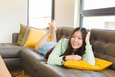 Genç Asyalı kadın gülümsüyor ve rahatlıyor, tatmin oluyor ve kaygısız, neşeli ve rahatlatıcı.