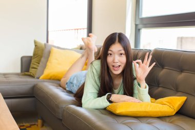 Genç Asyalı kadın kendini başarılı ve tatmin olmuş hissediyor, ağzı açık gülümsüyor, elle işaret veriyor.