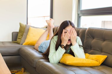 Genç Asyalı kadın korkmuş ya da utanmış hissediyor. Gözleri yarı kapalı ya da elleri kapalı dikizliyor ya da dikizliyor.