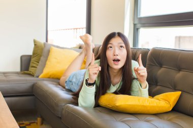 Genç Asyalı kadın korkuyla ve ağzı açık bir şekilde şaşkın ve şaşkın bir bakışla yukarıya bakıyor.