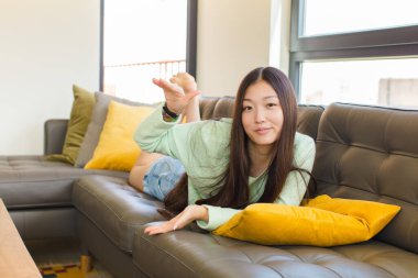 Genç Asyalı bir kadın iki eli de yan tarafında fotokopi alanı olan bir nesneyi tutuyor, bir nesneyi gösteriyor, sunuyor ya da reklamını yapıyor.