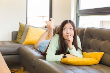 Genç Asyalı kadın düşünüyor, kuşkulu ve şaşkın hissediyor, farklı seçeneklerle, hangi kararı vereceğini merak ediyor.