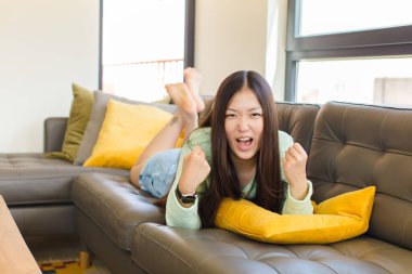 Asyalı genç bir kadın öfkeli bir ifadeyle bağırıyor ya da yumruklarıyla başarıyı kutluyor.