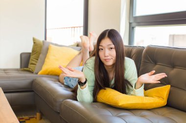 Genç Asyalı kadın şaşkın ve şaşkın hissediyor, doğru cevap veya karardan emin değil, bir seçim yapmaya çalışıyor.