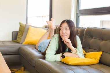 Genç Asyalı kadın düşünceli, meraklı ya da hayal kuruyor, hayal kuruyor ve uzayı taklit etmeye çalışıyor.