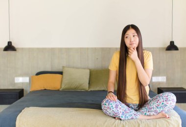 Genç Asyalı kadın düşünüyor, kuşkulu ve şaşkın hissediyor, farklı seçeneklerle, hangi kararı vereceğini merak ediyor.