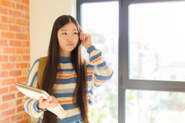 Genç Asyalı kadın kafası karışık ya da şüpheci, bir fikre odaklanmış, çok düşünüyor, kenarda boşluğu kopyalamak istiyor.