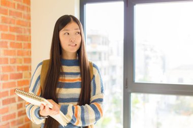 Genç Asyalı kadın kuşkulanıyor ya da düşünüyor, dudağını ısırıyor ve kendini güvensiz ve gergin hissediyor, kenarda boşluğu kopyalamak istiyor.