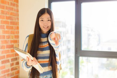 Genç Asyalı kadın kameraya tatmin olmuş, kendinden emin, dost canlısı bir gülümsemeyle bakıyor ve seni seçiyor.