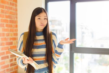 Genç Asyalı kadın şaşkın ve kafası karışık, şüpheci, farklı seçenekleri tartıyor ya da komik bir ifadeyle seçiyor.