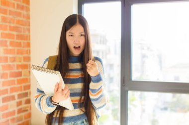 Asyalı genç bir kadın sinirli, sinirli, kızgın bakışlar ve sıkı yumruklarla bağırıyor. Öfkeli hissediyor.