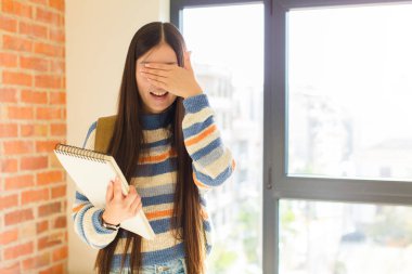 Genç Asyalı kadın gülümsüyor ve mutlu hissediyor, iki eliyle gözlerini kapatıyor ve inanılmaz bir sürpriz bekliyor.