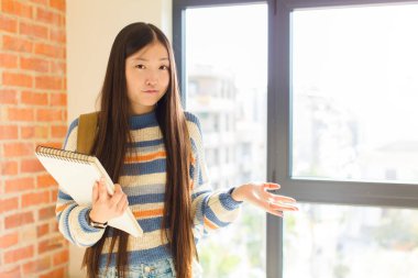 Genç Asyalı kadın şaşkın, şaşkın ve stresli görünüyor, farklı seçenekler arasında merak ediyor, kararsız hissediyor.