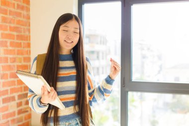 Genç Asyalı kadın gülümsüyor, kaygısız hissediyor, rahat ve mutlu, dans ediyor ve müzik dinliyor, bir partide eğleniyor.