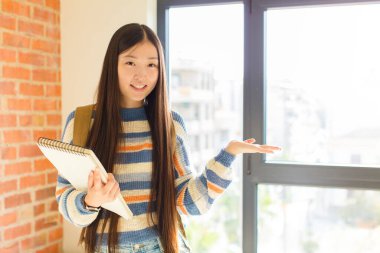 Genç Asyalı kadın gülümsüyor, kendinden emin, başarılı ve mutlu hissediyor, fotokopi alanında fikir veya konsept gösteriyor.