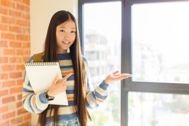 Genç Asyalı kadın gülümsüyor, mutlu, kaygısız ve tatmin olmuş hissediyor, fotokopi alanındaki konsepte ya da fikre işaret ediyor.