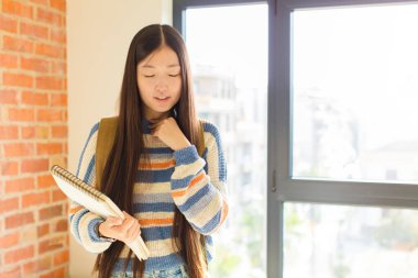 Genç Asyalı kadın boğaz ağrısı ve grip belirtileriyle hasta, ağzı kapalı öksürüyor.