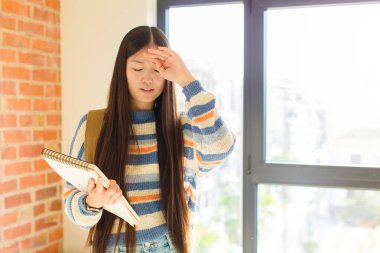 Genç Asyalı kadın stresli, yorgun ve hayal kırıklığına uğramış görünüyor, alnından ter akıyor, umutsuz ve bitkin hissediyor.