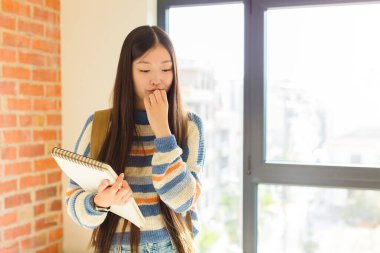 Asyalı genç bir kadın ciddi, düşünceli ve endişeli, elleri çenesine bastırılmış bir şekilde yan bakıyor.