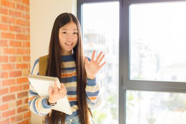 Genç Asyalı kadın gülümsüyor ve arkadaş canlısı görünüyor, 5 ya da 5 numarayı gösteriyor, eli önde, geri sayıyor.