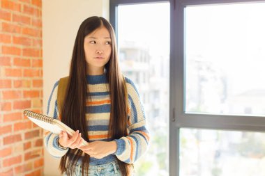 Asyalı genç bir kadın üzgün, üzgün ya da kızgın. Olumsuz bir tavır sergiliyor, anlaşmazlık içinde kaşlarını çatıyor.