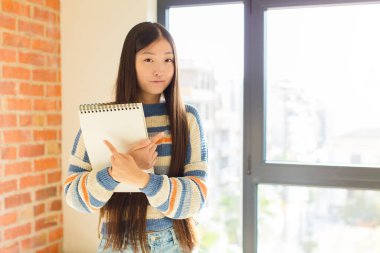 Genç Asyalı kadın şaşkın ve şaşkın görünüyor, güvensiz ve zıt yönlere şüpheyle bakıyor.