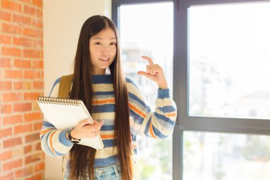 Asyalı genç bir kadın kendi gülüşünü çiziyor, iki eliyle, olumlu ve mutlu görünüyor, sağlık kavramı.