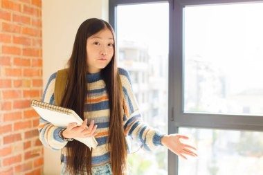 young asian woman feeling clueless and confused, having no idea, absolutely puzzled with a dumb or foolish look