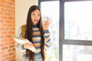 Genç Asyalı kadın kendini başarılı ve tatmin olmuş hissediyor, ağzı açık gülümsüyor, elle işaret veriyor.