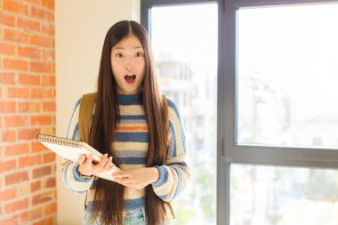 Genç Asyalı kadın korkmuş ve şok olmuş hissediyor, ağzı açık şaşkınlık içinde.