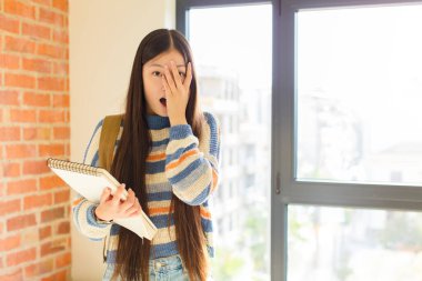 Genç Asyalı kadın korkmuş ya da utanmış hissediyor. Gözleri yarı kapalı ya da elleri kapalı dikizliyor ya da dikizliyor.