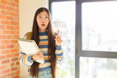 Genç Asyalı kadın korkuyla ve ağzı açık bir şekilde şaşkın ve şaşkın bir bakışla yukarıya bakıyor.