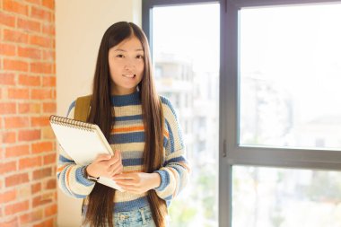 Genç Asyalı kadın şaşkın ve şaşkın görünüyor. Sinirli bir hareketle dudağını ısırıyor. Sorunun cevabını bilmiyor.