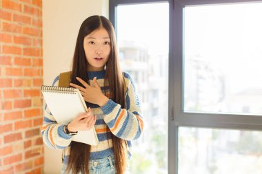 Genç Asyalı kadın şok olmuş ve şaşırmış hissediyor, gülümsüyor, el ele tutuşuyor, o olmaktan mutlu ya da minnettarlık gösteriyor.