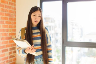 young asian woman feeling puzzled and confused, with a dumb, stunned expression looking at something unexpected