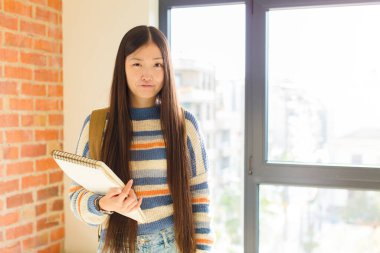 Genç Asyalı kadın kendini şaşkın ve kuşkulu hissediyor, merak ediyor ya da karar vermeye çalışıyor.