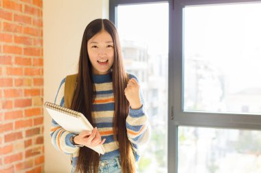 Genç Asyalı kadın zaferle bağırıyor, gülüyor, mutlu ve heyecanlı hissediyor başarıyı kutlarken.